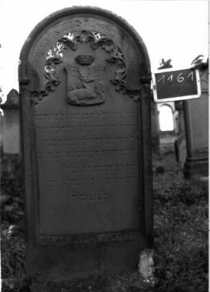 Grabstein 1161 (Index: 100104286) Material: Sandstein Zustand: gut erhalten, nur im Bogenbereich leicht verwittert Maße HxBxT: 170x70x18 cm Beschreibung: Stele mit Rundbogenabschluss, Verdachung, Schriftfeld eingetieft, im Bogenfeld Maßwerk (Rundbogenfries), darunter aufgesetztes Wappen mit Hirsch, drei Laubbäumen und Krone Symbolik: Wappen, Hirsch, drei Laubbäume, Krone, Rundbogenfries: Grabstein 1161