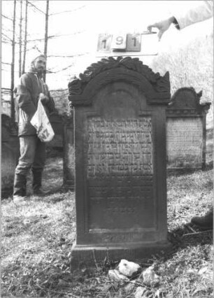Grabstein 191 (Index: 99608876) Material: Sandstein Zustand: stärker verwittert Maße HxBxT: 116x56x19 cm Beschreibung: Stele, profilierter Sockel, eingezogener Rundbogenabschluß mit floralem Aufsatz, Schriftfeld eingetieft mit floralem Aufsatz, Schriftfeld eingetieft mit eingezogenem Rundbogenabschluß: Grabstein 191