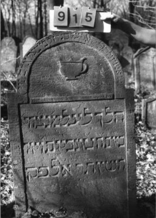 Grabstein 915 (Index: 99753215) Material: Sandstein Zustand: gut Maße HxBxT: 115x73x10 cm Beschreibung: Stele, eingezogener Rundbogenabschluß, rechteckiges Schriftfeld eingetieft Symbolik: Levitenkanne(eher Tasse): Grabstein 915