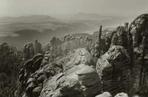 Sächsische Schweiz. Schrammsteine. Nördlicher Teil der Kette, Tante und Mittlerer Torstein von der Schrammsteinaussicht. Blick nach Südwesten über das Elbtal zum Kohlbornstein und Papststein