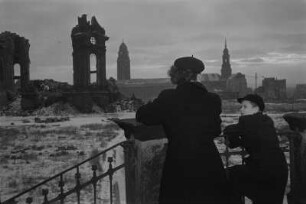 Dresden-Altstadt. Ruine der Frauenkirche. Frau mit Jungen (Bernd Zatschler) auf der Treppe des Johanneums (Verkehrsmuseum) stehend, im Hintergrund Rathaus mit Rathausturm und Turm der Kreuzkirche
