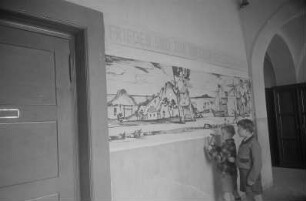 Dekorative Ausgestaltung der Klassenräume und Schulflure in der Einheitsschule Baumschulenweg und Oberschule Niederschöneweide in Vorbereitung des Deutschlandtreffens der Jugend für Frieden und Völkerfreundschaft zu Pfingsten 1950 : Schüler bringen ein Plakat zum Deutschlandtreffen an einer Wand im Hausflur einer Schule an