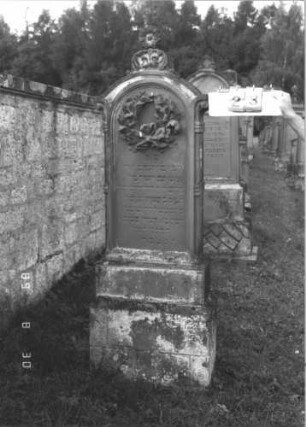 Grabstein 23 (Index: 99609659) Material: Sandstein Zustand: verwittert Maße HxBxT: 189x63x24 cm Beschreibung: Stele, Segmentbogenabschluß, in Voluten auslaufend, Volutenaufsatz, Blüte, Schriftfeld eingetieft, getreppter Sockel Symbolik: Kranz, Blüte: Grabstein 23