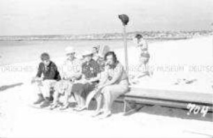 Touristen auf einer Bank am Strand sitzend
