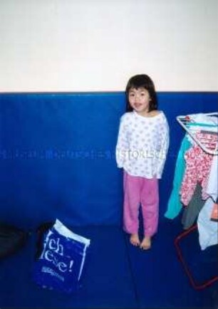 Kleines asiatisches Mädchen vor blauer Wand mit Wäscheständer (Sonderthema: Familienbilder)