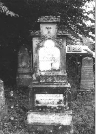 Grabstein 122 (Index: 99800074) Material: Sandstein, Schriftplatten Marmor Zustand: verwittert, Schriftplatte gesprungen Maße HxBxT: 162x56x24 cm Beschreibung: Stele, Mittelerhöhung, Zinnenaufsatz, eingelassene Schriftplatte mit Kleeblattbogenabschluß, getreppter Sockel, im oberen Teil weitere Schriftplatte eingelassen: Grabstein 122