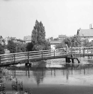 Trave: Hochwasser: vorn links Grünpflanzen: in der Mitte Kranbrücke: darauf Frau mit Fahrrad: hinten rechts Gebäude der Hamburger Tapetenfabrik: dahinter Gasometer der Stadtwerke: hinten links hinter Bäumen Häuser an der Lübecker Straße