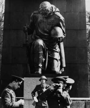 Sowjetische Soldaten vor einer der beiden Bronzeskulpturen eines knieenden Soldaten der Sowjetischen Armee vor roter Granitwand am Hauptweg