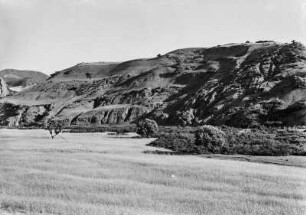 Landschaft : Durch Erosionsrisse zerklüftete Hänge, davor Weizenfelder und Weiden