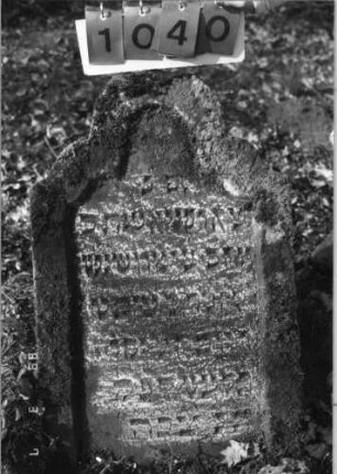 Grabstein 1040 (Index: 99751170) Material: Sandstein Zustand: stark verwitt/Stele nach hinten gekippt Maße HxBxT: 92x56x9 cm Beschreibung: Stele, geschwungen, eingezogener Rundbogenabschluß, Schriftfeld eingetieft: Grabstein 1040