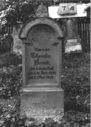 Grabstein 74 (Index: 100106509) Material: Sandstein Zustand: verwittert, Ornament nachgemalt Maße HxBxT: 107x44x15 cm Beschreibung: Stele mit überkragendem Rundbogenabschluß, Verdachung, Schriftfeld eingetieft mit eingezogenem Rundbogenabschluß, Sockel Symbolik: Stern, floral: Grabstein 74