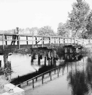 Trave: Holzbrücke "Grüne Brücke": links darauf Fußgänger am Geländer: vorn links Angeln über dem Wasser: hinten Baumgruppen