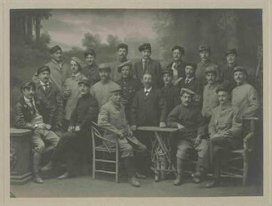 21 Kriegsgefangene, teils stehend, teils sitzend in Atelier positioniert vor gemalter Waldlichtung, Kriegsgefangenenlager Ludwigsburg-Eglosheim