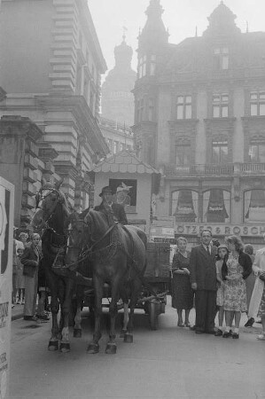 Ein Pferdefuhrwerk sowie Passanten auf einer Straße während der Leipziger Herbstmesse 1955