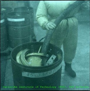 Mitarbeiter im Schutzanzug beim Befüllen eines Behälters mit radioaktivem Material in der Hauptabteilung Dekontaminationsbetriebe (HDB)