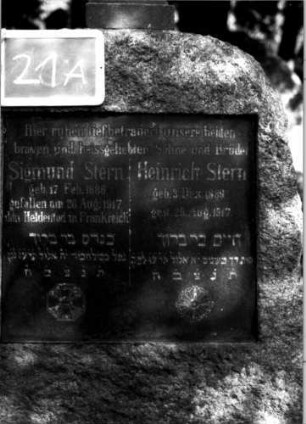 Grabstein 21 (Index: 100110062) Material: Granit Zustand: gut Maße HxBxT: 190x83x45 cm Beschreibung: konische Stele, Korbbogenabschluß, Schriftplatte rechteckig Symbolik: Eisernes Kreuz mit Davidstern und Lorbeerkranz, stilisierte Blüte, Urne mit Kranz als Aufsatz Besonderheit: Doppelgrab: Grabstein 21A