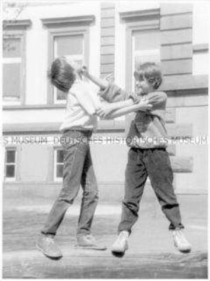 Zwei Jungen balgen sich im Schulhof auf einem Balken (Altersgruppe bis 14)
