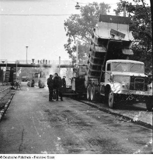 Straßenbau in Höhe Industriegelände. Aufbringen von Heißmischgut und Herstellen der Fahrbahndeckschicht