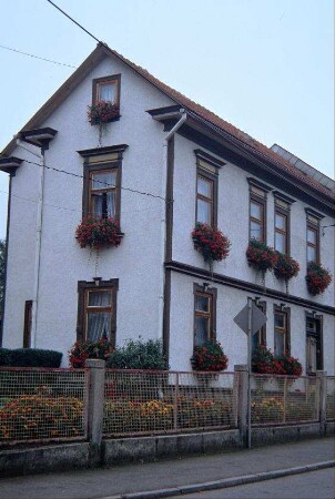 schmales Wohnhaus mit hohen Fenstern, Blumenkästen; Garten