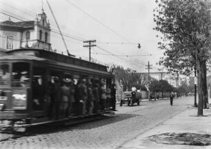 Straßenbahn : Ein vollbesetzte Tram fährt eine Straße entlang. Im Hintergrund Wohnhäuser.