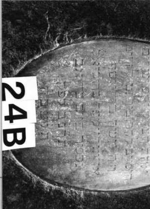 Grabstein 24 (Index: 100081755) Material: Granit, weiße Marmorplatten Zustand: Schriftplatten verwittert mit Textverlus Maße HxBxT: 163x65x34 cm Beschreibung: leicht konische Stele, schräger Abschluß, ovale und querrechteckige Schriftplatten: Grabstein 24B