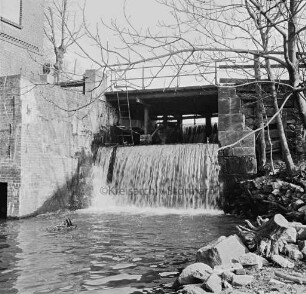 Mühlenwehr zwischen Mühlenteich und Glinder Au: darüber baufällige Brücke der Mühlenstraße: rechts Bäume: links Mühlengebäude