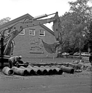 Abwasser: Ausbau der Kanalisation: Wöhrendamm: vorn Röhren: dahinter Baugrube: links Arbeiter und Bagger: rechts weiterer Arbeiter: hinten links Waldreitersaal mit Relief an Giebelfront: hinten rechts parkende Pkws und Bäume