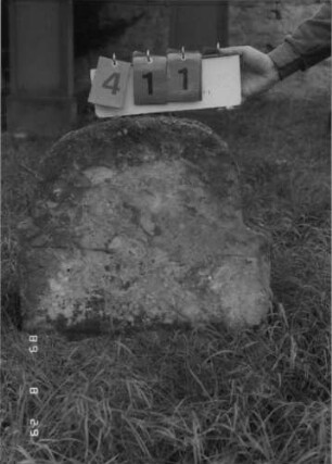 Grabstein 411 (Index: 100107914) Material: grauer Sandstein Zustand: völlig verwittert und abgeblättert, keine Textreste Maße HxBxT: 63x64x10 cm Beschreibung: Stele, eingezogener Rundbogenabschluß: Grabstein 411