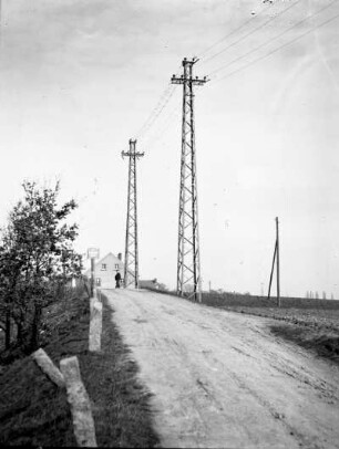 Sachsen? Erste 110 kV-Freileitung des Elektroarmaturenwerks Radebeul-Kötzschenbroda. Dorfstraße mit Leitungsmasten. Blick gegen Wohnhaus