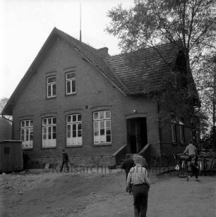 Volksschule: Schulkoppel: altes Schulgebäude: vorn Schulkinder: rechts Fahrradständer mit Fahrrädern: dahinter Bäume: links Baubude