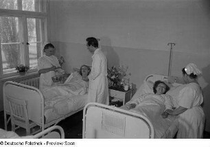 Blick in ein Krankenzimmer mit Arzt, Krankenschwestern und Patienten