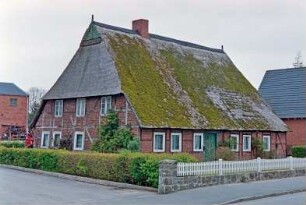 Hauptstraße (7): traufständige Fachwerkkate mit Reetdach: Straßenfront mit Eingangstür: Giebelseite Wohntrakt: Gartenzaun, Hecke, links Einfahrt: hinten Wirtschaftsgebäude