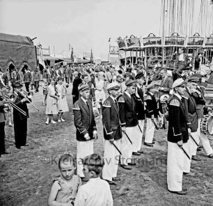 Schützenfest: Veranstalter Bürgerschützengilde von 1627 e.V. Bad Oldesloe: Umzug: Aufmarsch auf Festplatz an Sehmsdorfer Straße: Fanfarenzug der Deutschen Jugend des Ostens, Schützenkapelle, Schützenvereine mit Fahnen: Zuschauer und Festbesucher, im Vordergrund zwei kleine Kinder: Kinder auf Kettenkarussell, hinten Kinderkarussell, Jahrmarktstände