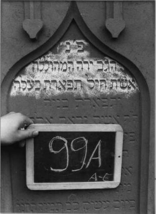 Grabstein 99 (Index: 99937115) Material: Sandstein Zustand: gut Maße HxBxT: 170x61x30 cm Beschreibung: ädikulaartige Stele mit Halbsäulen, profilierter Sockel, Giebel mit stilisierten Eckakroteren, Schriftfeld eingetieft mit Rundbogenabschluß Symbolik: Maßwerk mit herabhängenden Herzen, Voluten und Efeuranken im Giebel: Grabstein 99A (Nachholaufnahme)