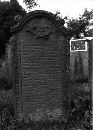 Grabstein 453 (Index: 100102717) Material: Sandstein Zustand: gut erhalten, im Bogenfeld teilweise verwittert Maße HxBxT: 176x85x16 cm Beschreibung: Stele, Konvexbogenabschluss mit Verdachung, auf den Einzügen Kugelaufsätze, im Bogen gekreuzte Akanthusblätter, Seitenränder mit Blütenfries Symbolik: gekreuzte Akanthusblätter, Blütenfries: Grabstein 453