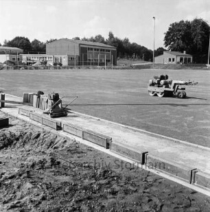 Oetjendorfer Landstraße / Waldweg: Turn- und Sportverein Hoisdorf: Sportzentrum: Anlage eines Sportplatzes: vorn Gehweg im Aufbau: links Rüttler und Stapel Gehwegplatten: rechts Walze: hinten links Turnhalle, rechts Umkleidehaus: dahinter Bäume