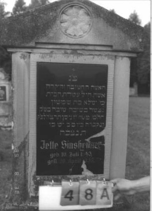 Grabstein 48 (Index: 99609684) Material: Sandstein Zustand: verwittert, Schriftplatte Glas? gesprungen Maße HxBxT: 186x67x27 cm Beschreibung: Stele, überkragender Giebelabschluß, eingelassene rechteckige Schriftplatte, getreppter Sockel Symbolik: Rosette: Grabstein 48A