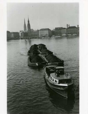 Hamburg. Ein mit Kohle beladener Schleppverband auf der Alster. Im Hintergrund die Silhouette der Freien- und Hansestadt
