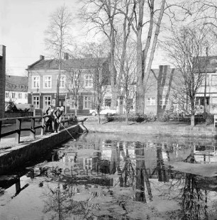 Feuerlöschteich ("Pansenteich"): hinten Rathausstraße, an Ecke Mittelweg: Mann mit Kescher am Geländer, zwei Jungen als Zuschauer: hinten links Gasthaus Jägerstube, rechts daneben Schlachterei Wunder