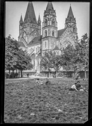 Kirche, Ansicht - vorne ein Park, in dem Menschen auf dem Rasen sitzen