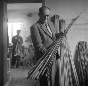 Spangenberg. Porträt eines Mannes mit Peitschen. Im Hintergrund Peitschenmacher bei der Arbeit