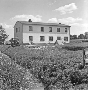 Altes Torfredder: Mehrfamilienhaus [ehemaliges Gefängnis Nienwohld]: links davor Trecker und Pkw, rechts Zelt und Schaukel im Garten: im Vordergrund Graben mit Stauden