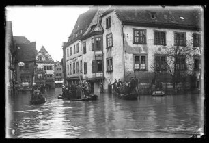Hochwasser in der Brückengasse Richtung Marktplatz vor Chorstift-Drogerie F. Schwender, Pelz- und Modewaren Johanna Strauß u.a. sowie Brunnen, darauf Personen in Schelchen