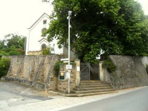 Ansicht von Südwesten mit Langhaus (Retrostil romanisch) über Kirchhofmauer (mit Strebepfeilern)