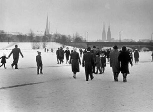 Hamburg im Winter. Spaziergänger laufen über das Eis der zugefrorenen Außenalster. Im Hintergrund die Silhouette der Innenstadt