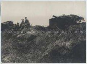 Soldaten und zerschossene Panzer vor einem deutschen Schützengraben