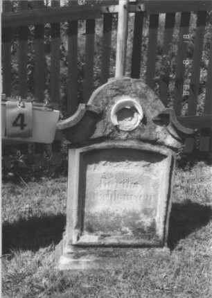 Grabstein 4 (Index: 100105127) Material: Sandstein Zustand: sehr stark verwittert, Einsatz im Giebel zerstört Maße HxBxT: 64x42x19 cm Beschreibung: Stele auf getrepptem Sockel, eingezogener Giebel mit konkaven Abschlüssen und rundem Einsatz (zerstört), vertiefter Textteil Symbolik: zerstört: Grabstein 4