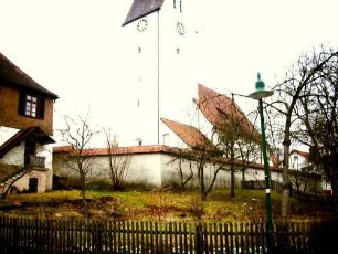 Ansicht von Nordosten mit Kirche (im Kern Spätromanisch) über Kirchhofmauer (Wehrgang im 19 Jh abgetragen) im leicht erhöhter Lage am Ortsrand