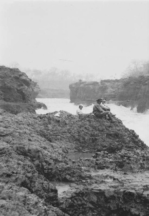 Der "Ferrador" des Rio Grande : Einige Expeditionsteilnehmer sitzen auf Felsen am Ufer des Rio Grande, danben der "Ferrador" des Rio Grande mit Stromschnellen.