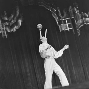 Auftritt eines Jongleurs in einem Varieté, der mit seinem Gesicht einen Ball auf einer Keule balanciert